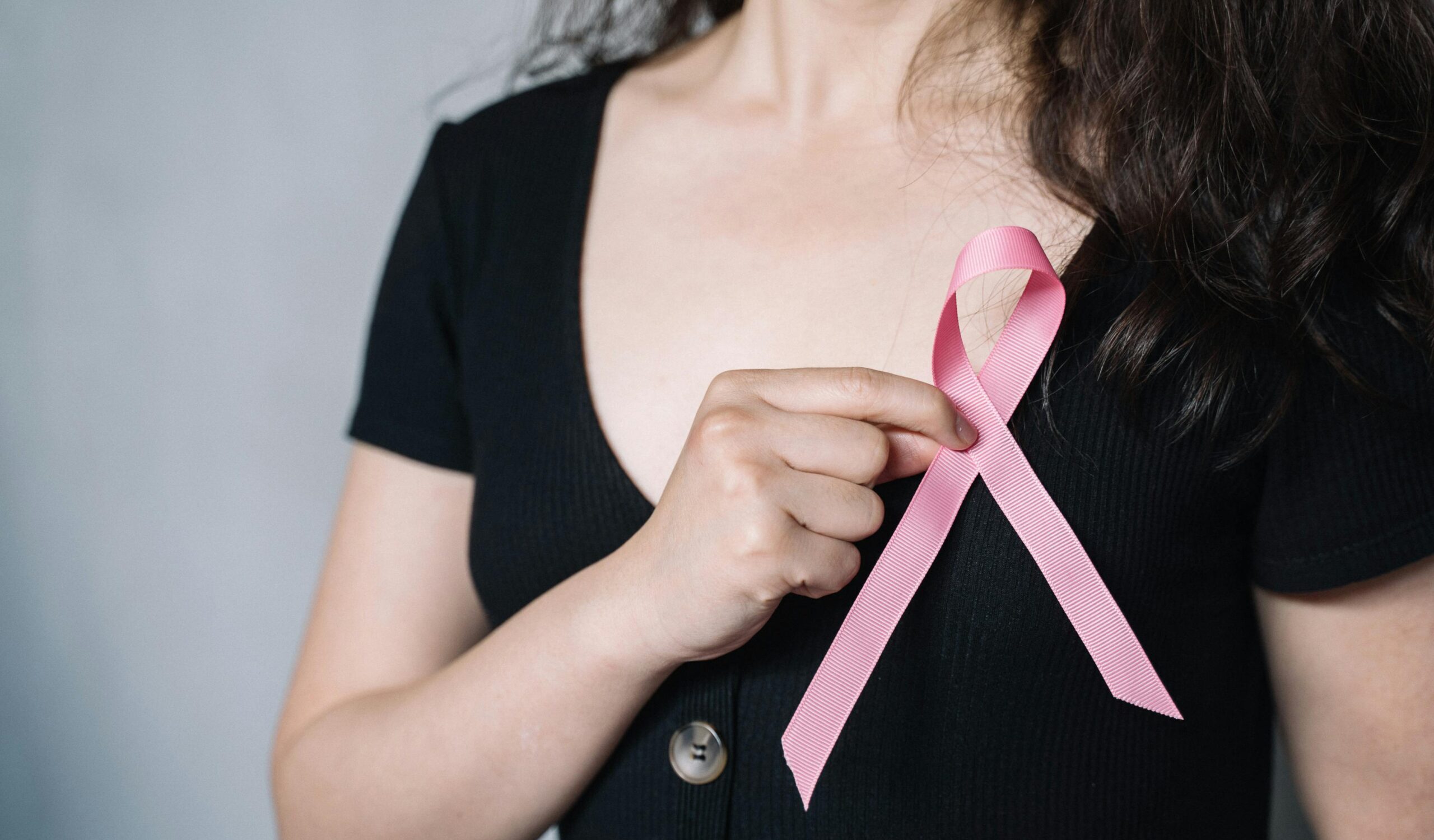 Close-up of a woman holding a pink ribbon symbolizing breast cancer awareness and support.